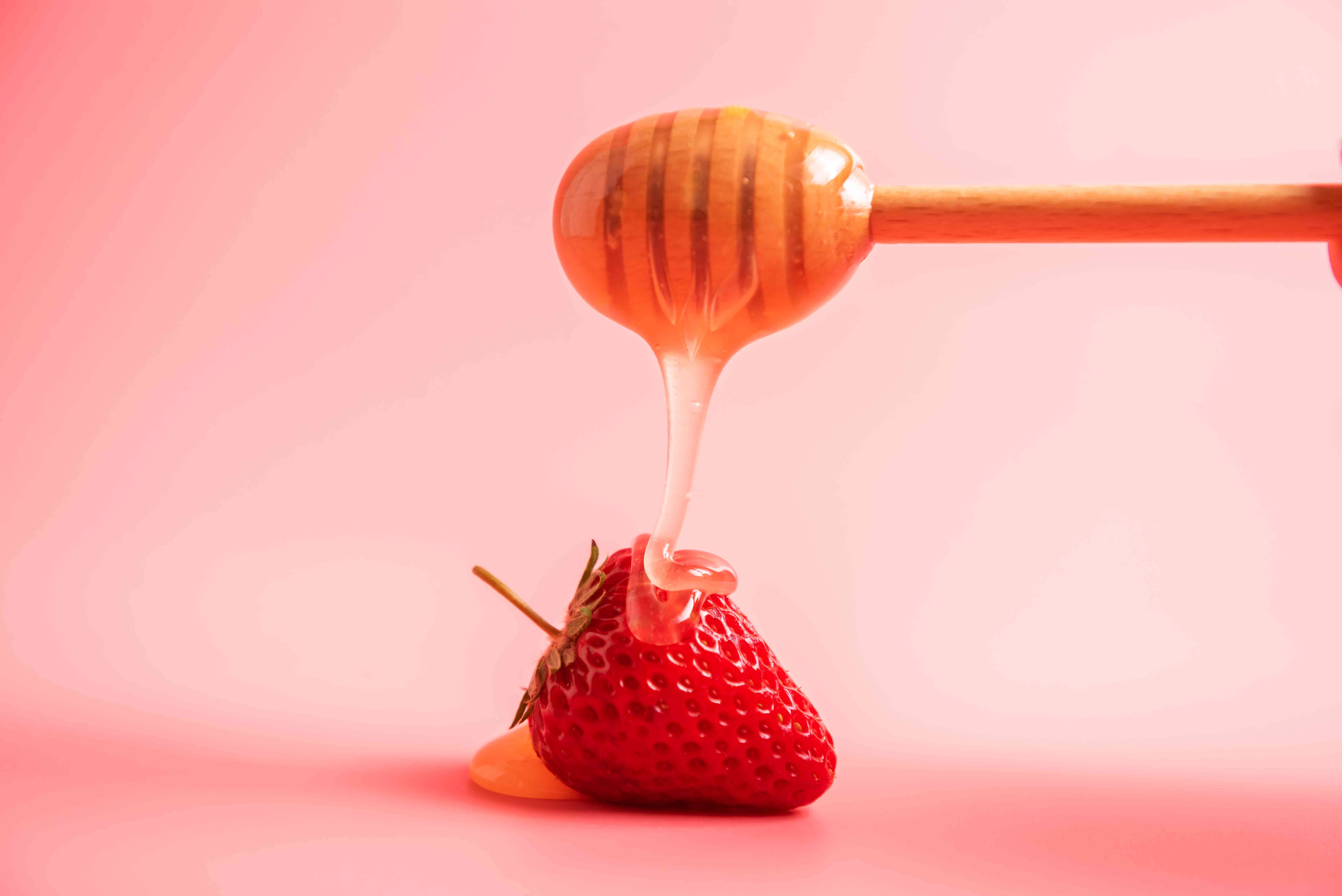 蜂蜜滴在草莓上，粉红色的背景