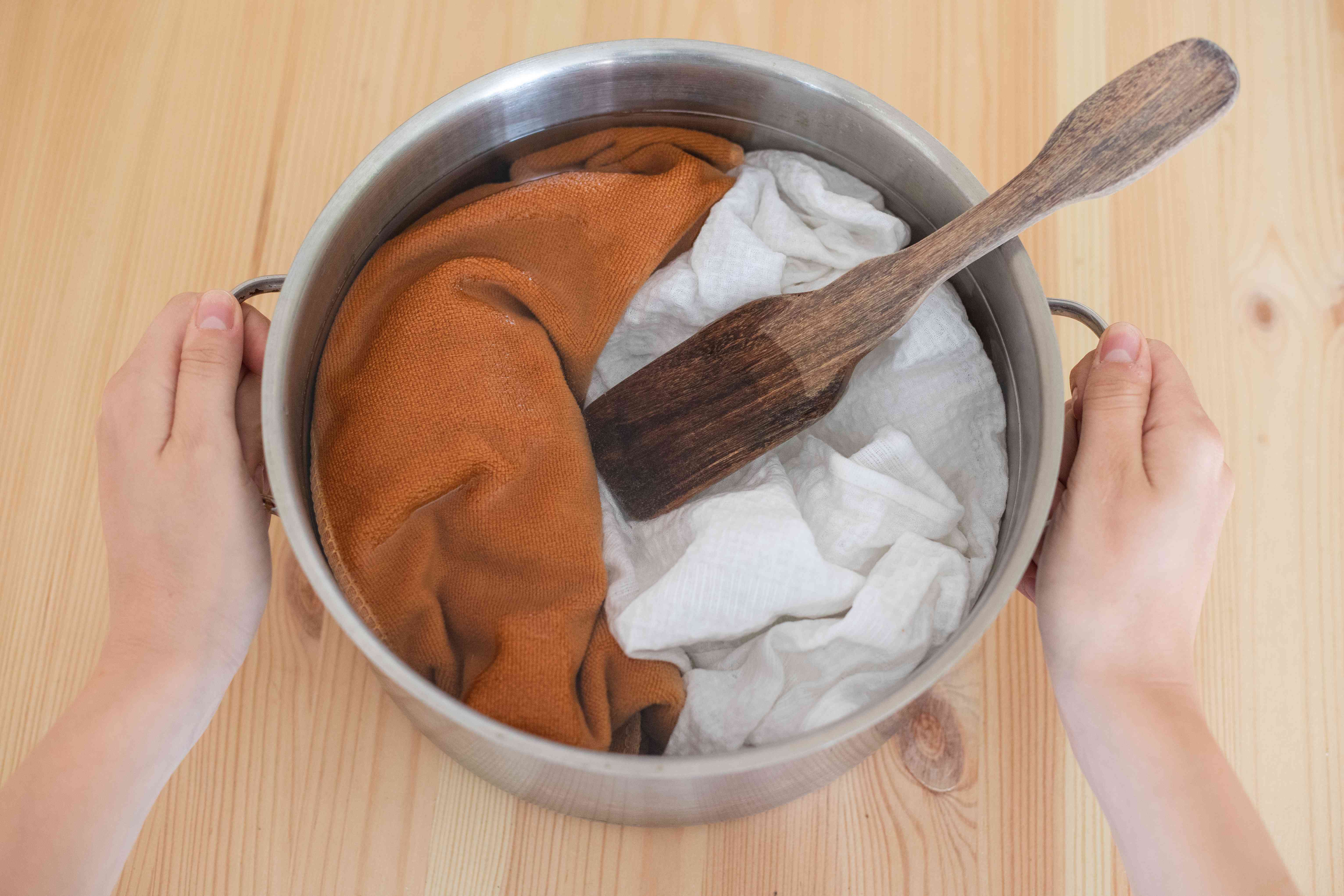 衣服在钢制汤锅中浸泡在醋水混合物中，用手握住两边