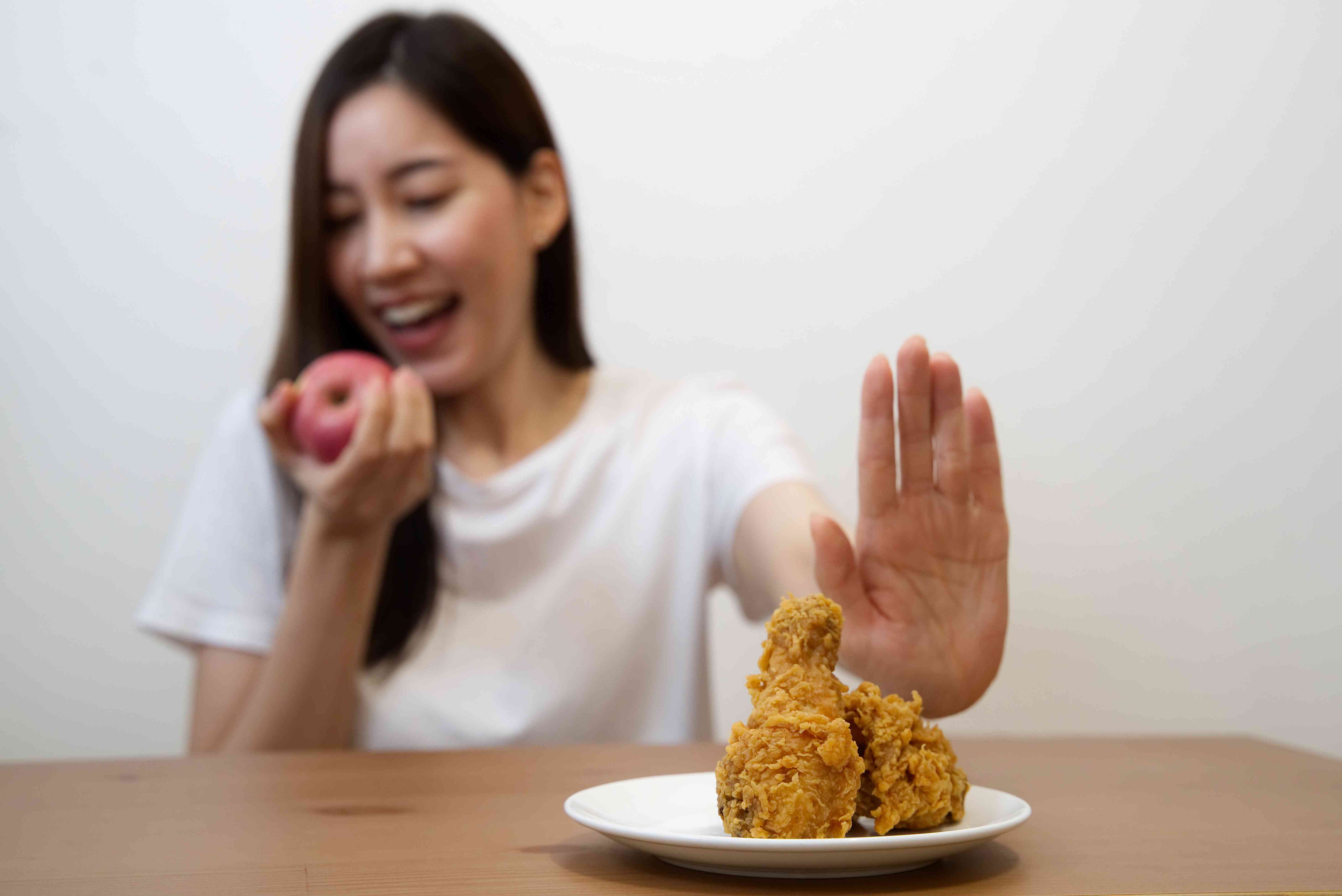 年轻女孩在节食对身体健康的概念。关闭女性使用手拒绝垃圾食品推出她最喜欢炸鸡和为健康选择红苹果和沙拉。