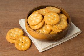 木碗中的圆形咸饼干饼干，放在亚麻和木制背景上。