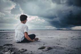 男孩独自坐在暴风雨的海滩上