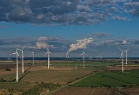 在这张鸟瞰图中，当水蒸气从德国Weissenfels附近的Kraftwerk Lippendorf燃煤发电站的冷却塔上升时，风力涡轮机在风力公园旋转。
