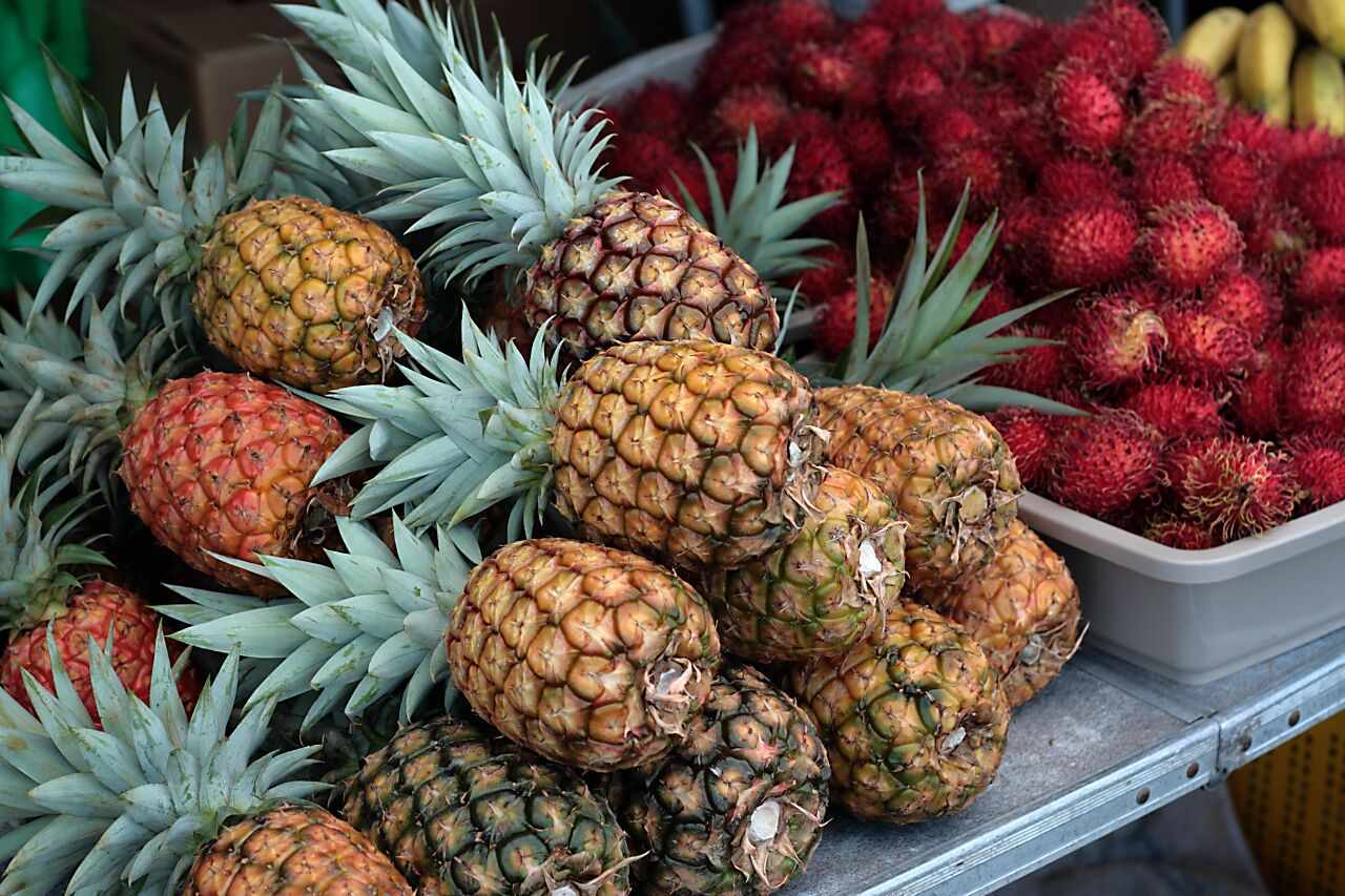 农贸市场桌上的菠萝和红毛丹的特写＂width=