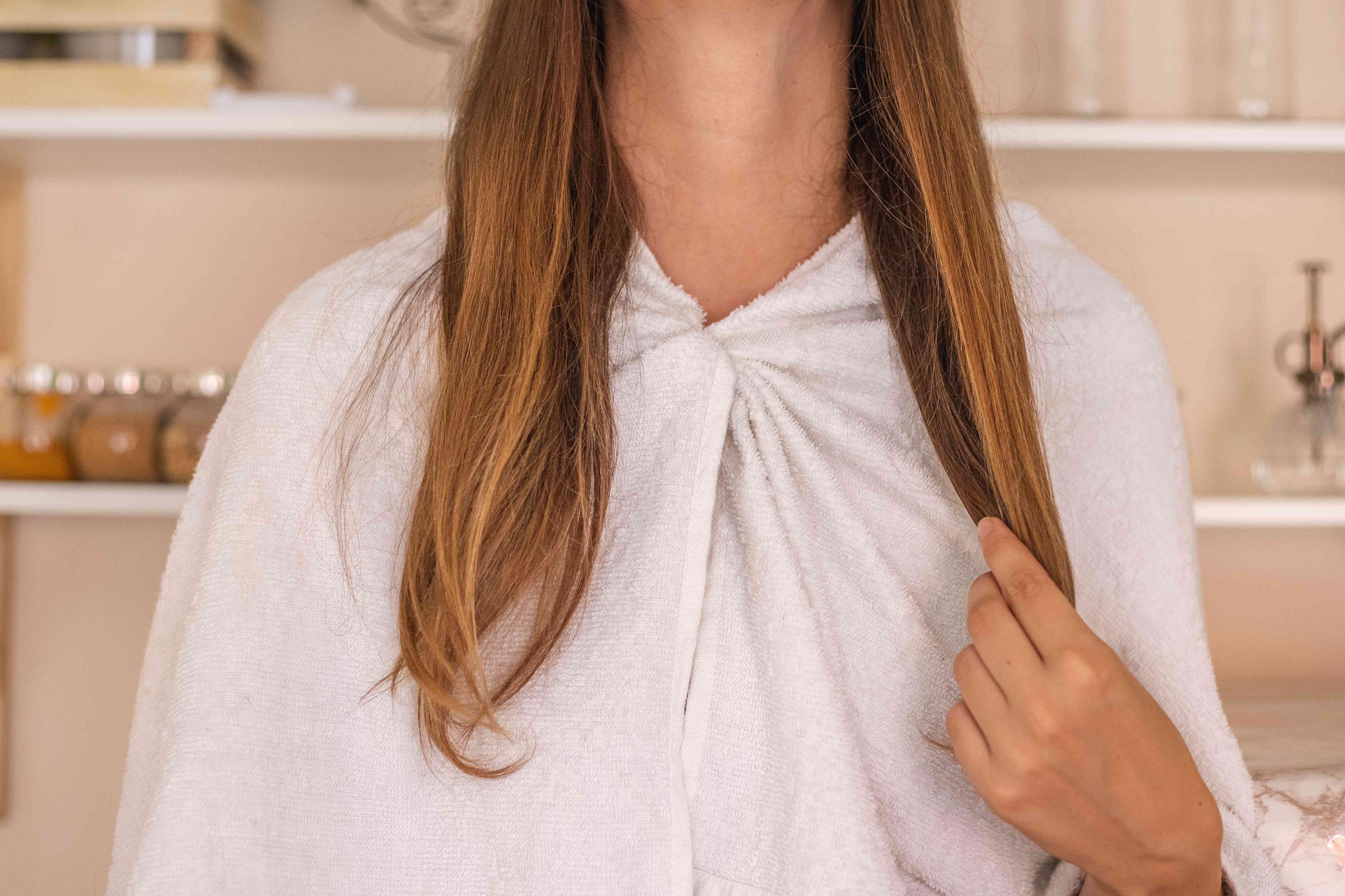 一位女士用毛巾裹住肩膀，将橄榄油面膜敷在长发上