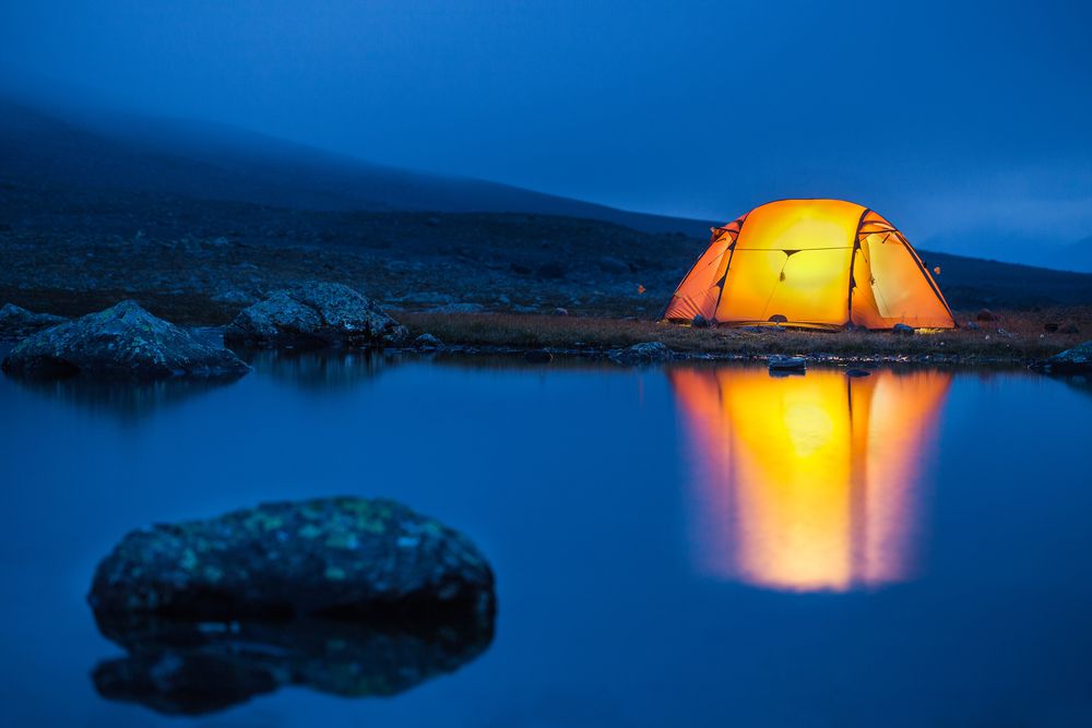帐篷里舒适的光线反射出池塘里平静的湖水，使它的光线更加明亮。