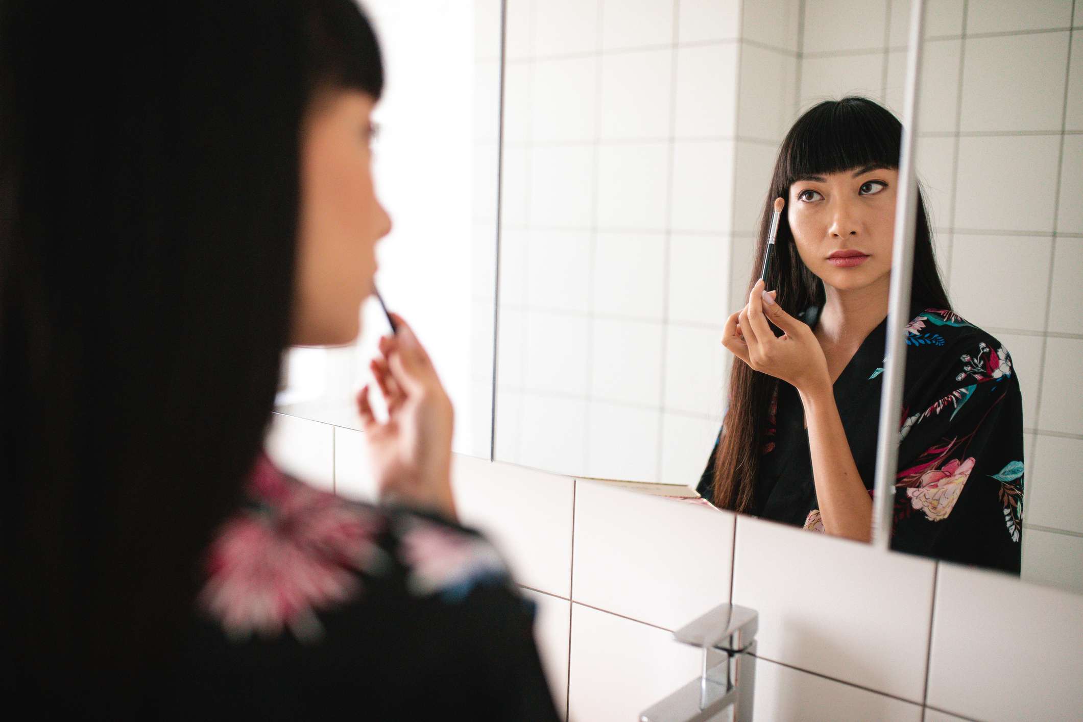 一个有刘海和长发的亚洲女人在镜子里涂抹眼影。