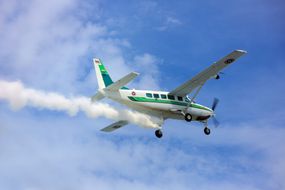 Close-up of a turboprop plane sprinkling chemicals into clouds in a blue sky.