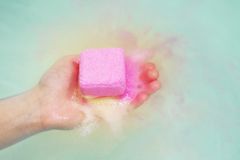 一只白色的手拿着水中的粉色和黄色的沐浴炸弹。