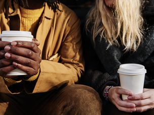 多元文化的不可识别的朋友坐在一起时拿着一杯咖啡。专注于手
