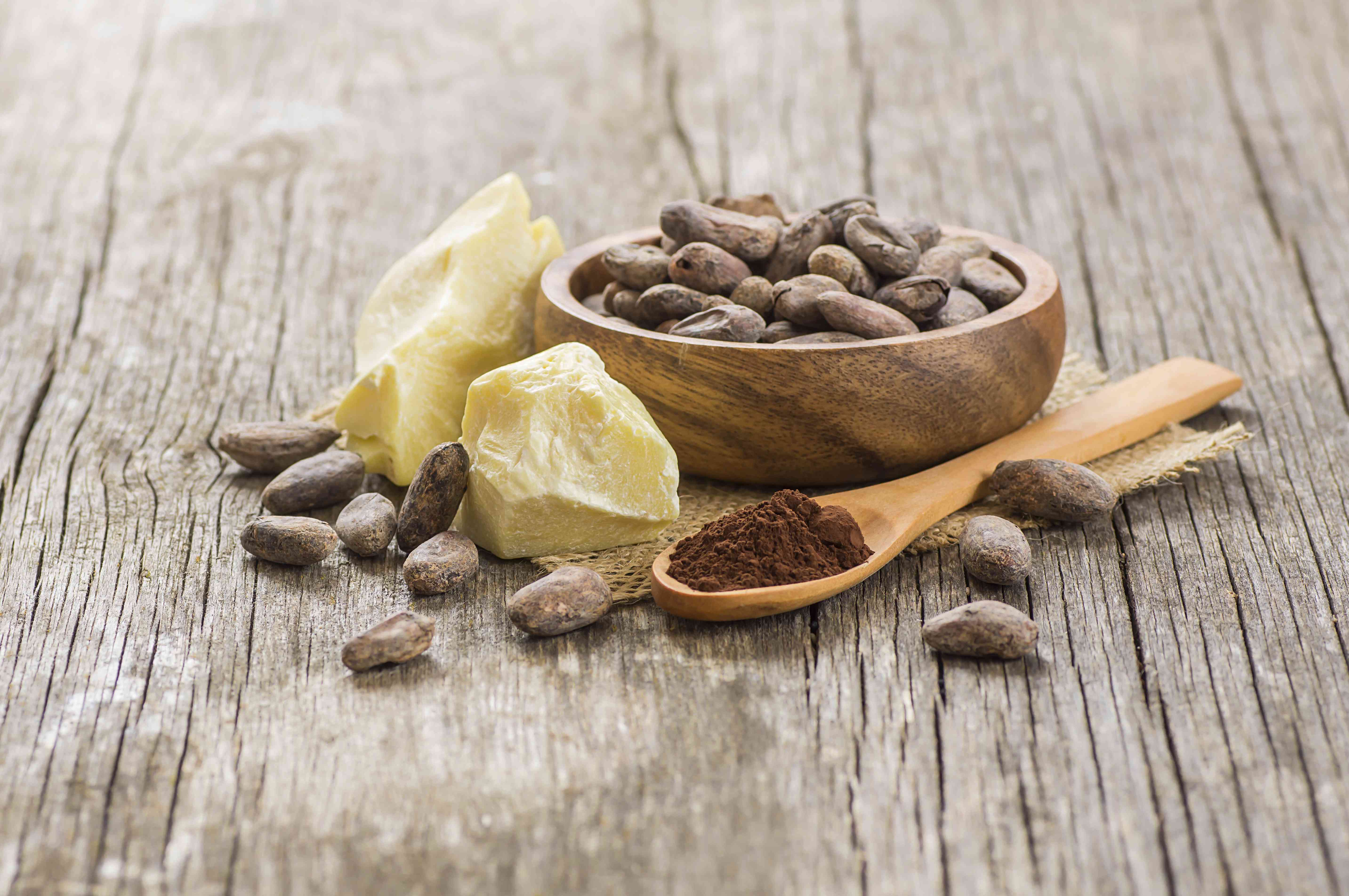 可可脂或可可豆固体油与可可粉在勺子和生可可豆在木碗在乡村背景。