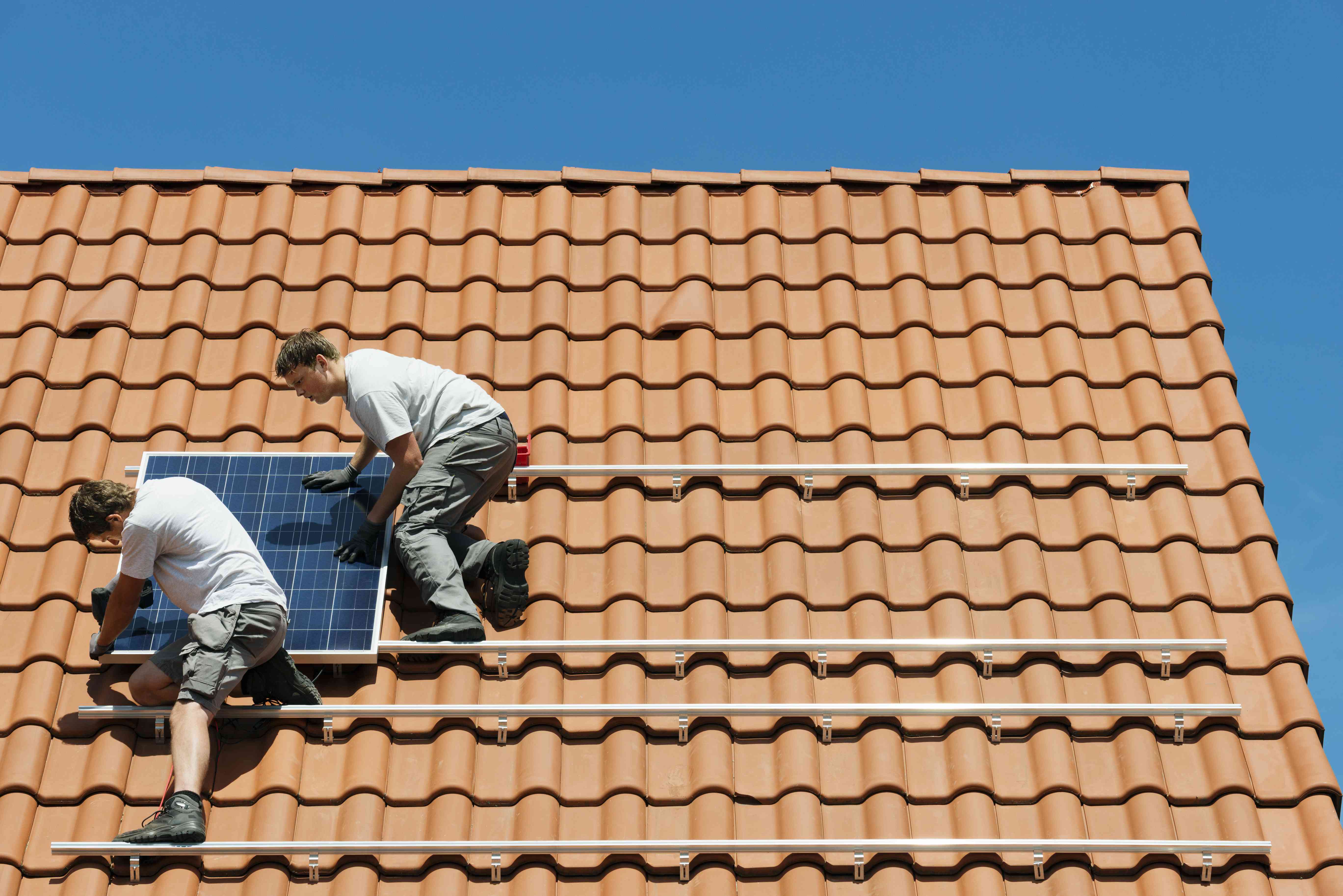 荷兰，工人们在新房子的屋顶框架上安装太阳能电池板＂width=