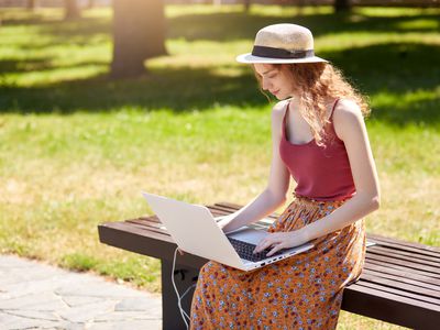 女人坐在公园的长椅上用她一个太阳能充电器的笔记本电脑