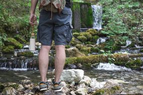 一个带着水瓶和背包的人在瀑布附近的岩石小溪远足