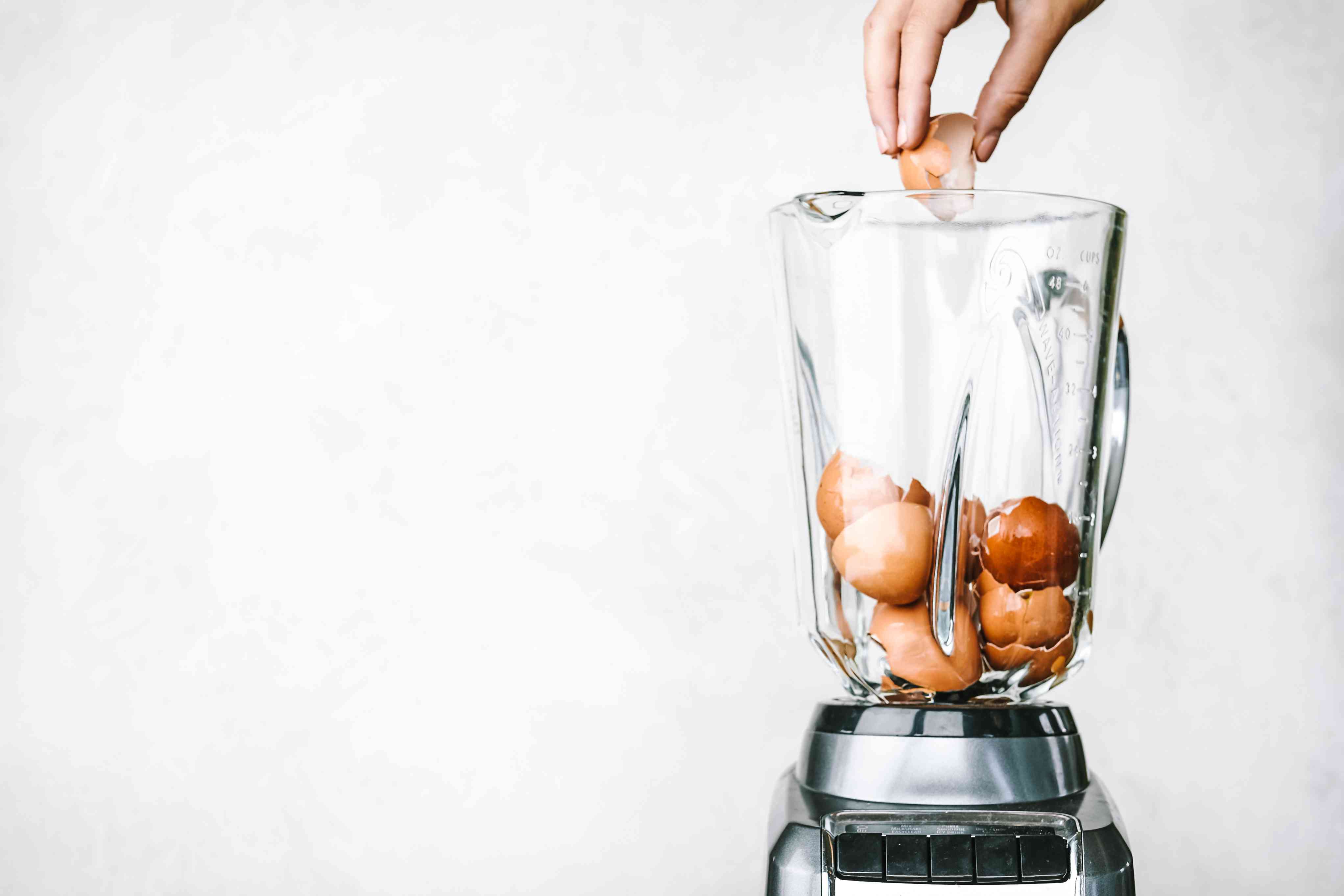 手把碎蛋壳扔进玻璃搅拌机里，里面装满了棕色的蛋壳