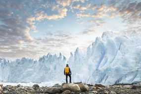 日落时分，一座冰川高耸在徒步旅行者的头顶上。＂width=