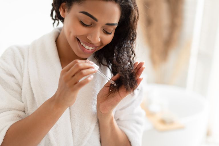 应用在损坏的干燥头发的非裔美国人的妇女血清在现代卫生间里在家。