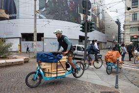 两个周期快递员在提供食物时骑着货物自行车。“width=