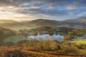 日出时Loughrigg Tarn的山丘和秋天的树木