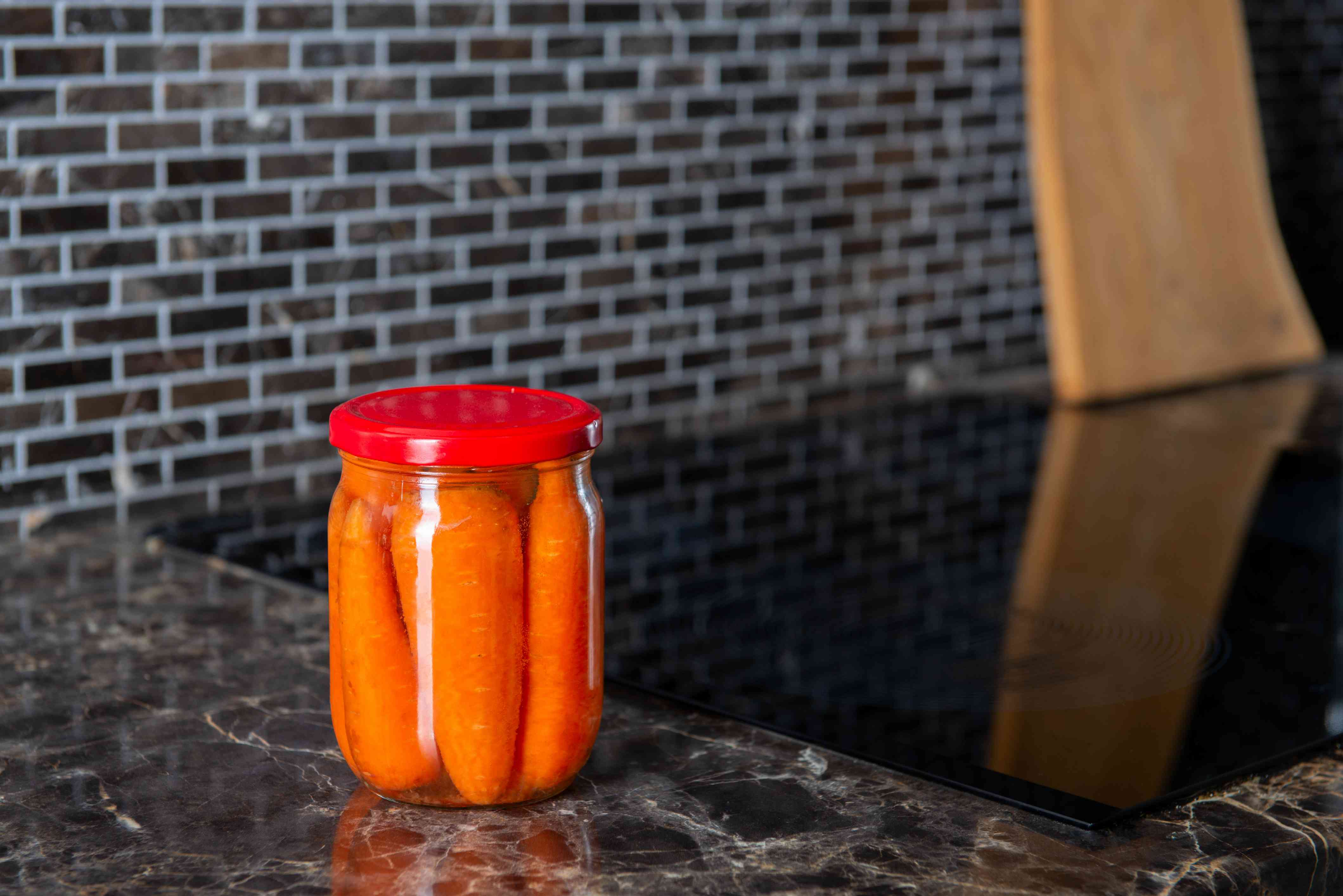 腌制胡萝卜保存在玻璃罐中，红色的顶部放在厨房柜台上