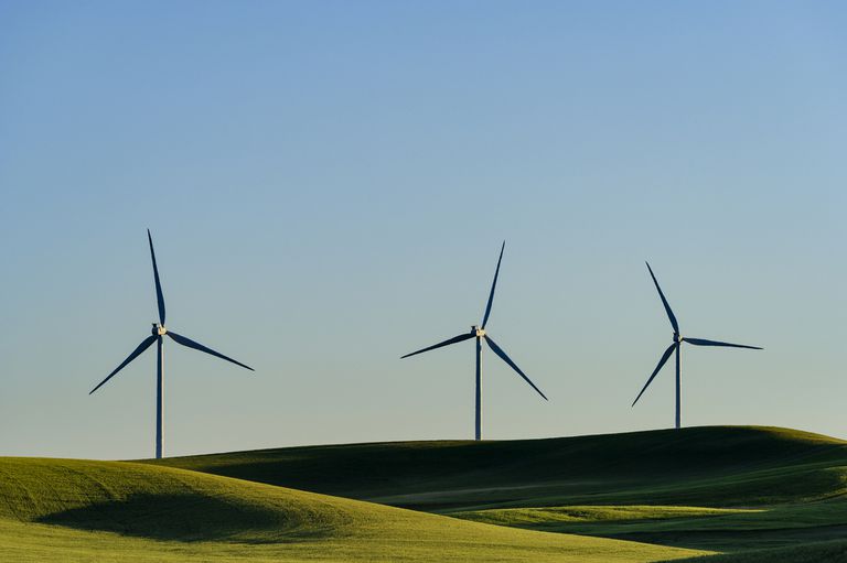 三个风力涡轮机在起伏的山丘和蓝天上。